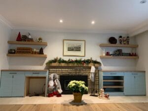 Complete living room view showcasing symmetrical blue entertainment cabinets with floating wood shelves surrounding stone fireplace by Polymita Woodcraft