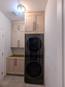 Compact laundry room featuring floor-to-ceiling natural wood cabinets surrounding stacked washer-dryer unit by Polymita Woodcraft